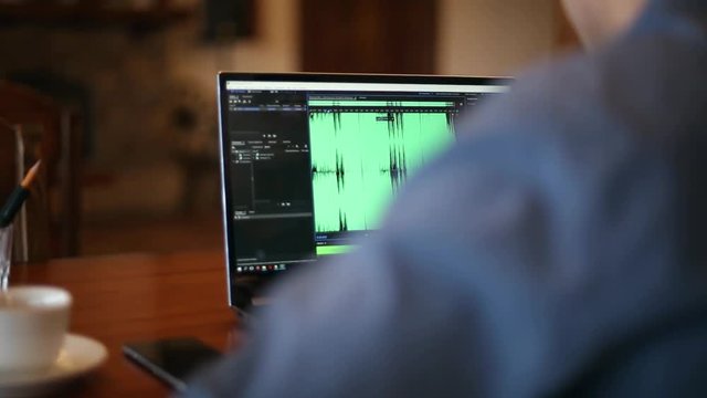 Sound designer or engineer working on laptop with audio mastering software with waveform on screen. Dj man listening to music. Tracking and revealing shot.