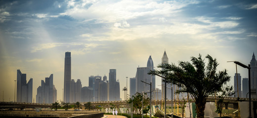Panoramic view of business bay, downtown area of Dubai and two arab men take a walk on the promenade at cloudy day. UAE