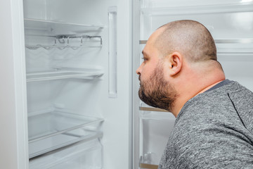 Fat hungry man is looking for a food into empty fridge