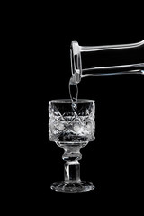 A faceted glass of vodka is pouring vodka from a carafe.