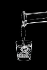 A small shot of vodka is pouring vodka from a carafe.