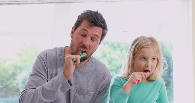 Smiling father and daughter brushing teeth  
