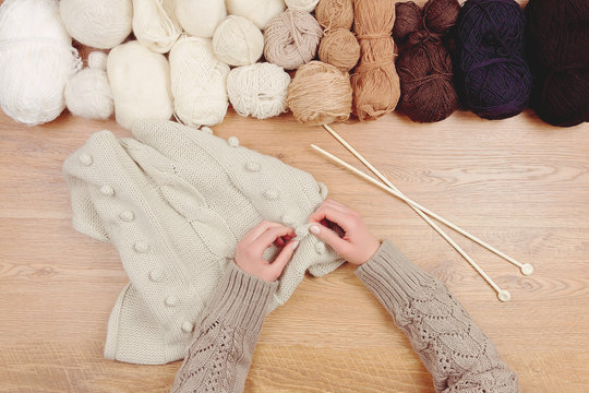 Dressmaker workplace. Woman female girl hands knitting warm sweater by knitted needles on wooden background with line of balls of thread