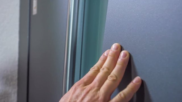 A businessman is touching the exterior of the front door very gently. He also touches the handle.