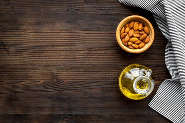 Oil for skin care. Almond oil near almond on dark wooden background top view copy space