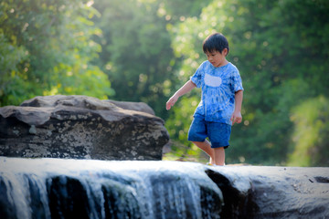 A boy standing on a rock with a waterfall in a rain forest on a mountain.