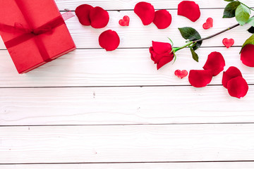 Prepare the prsesnts or surprise for Valentine's day. Red gift box near red rose and petals on white wooden background top view copy space