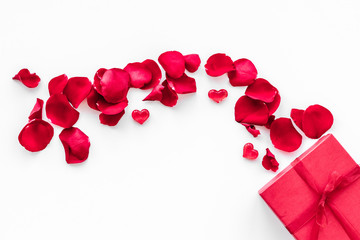 Gift for Valentine's day. Red gift box near red rose petals on white background top view copy space