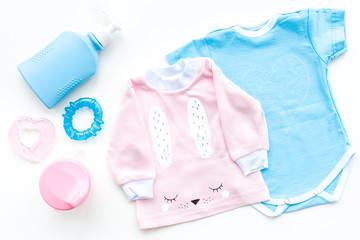 Baby clothes concept. Blue bodysuit for boy and pink shirt for girl near baby accessories on white background top view
