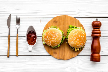 Burger on wooden cutting board on white wooden background top view