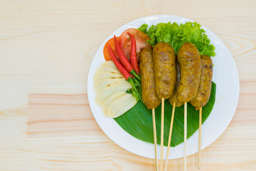 The delicious Thai Fermented Sausages
(Sai Krok Isan) with side dishes from northeastern of Thailand on wooden table background.