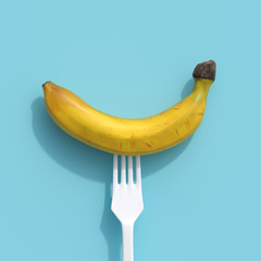 banana on a white fork on blue background. creative idea concept.