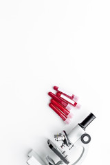Blood analysis in clinacal lab. Test tubes near microscope on white background top view copy space