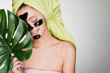 happy woman with a towel on her head applied a mask to problem areas of the face