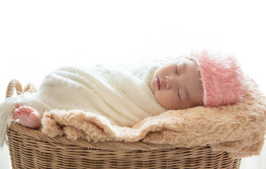 Newborn baby boy sleep on his brown basket relaxing under a white wrap cloth and pink hat