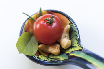 Little tomato with some cashew nuts, basil and rosemaries on a beautifully illustrated spoon.