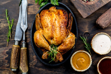 Roasted chicken with rosemary served on black plate with sauces on wooden table, top view. © lblinova