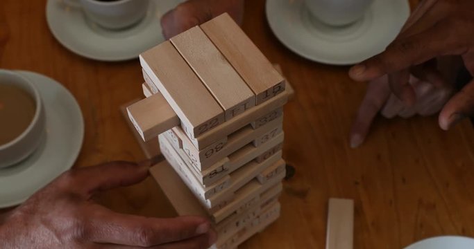 Friends playing jenga game on table while having coffee in bar 