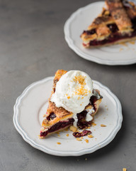 A piece of cherry pie with vanilla ice cream on a white vintage plate on a gray light concrete background. Copy Space. View blank space for text.