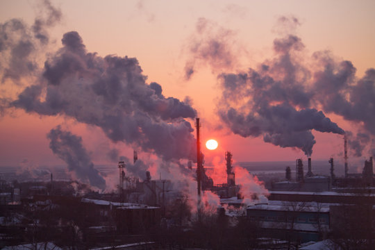 the chimneys of a refinery with smoke and steam with the pinkk sunset on the background