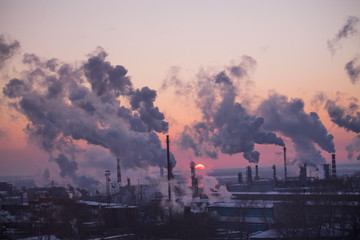 the chimneys of a refinery with smoke and steam with the pinkk sunset on the background