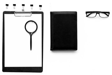 Strict monochrome white and black office desk table with pad, magnifier, notebook, glasses on white background top view copy space