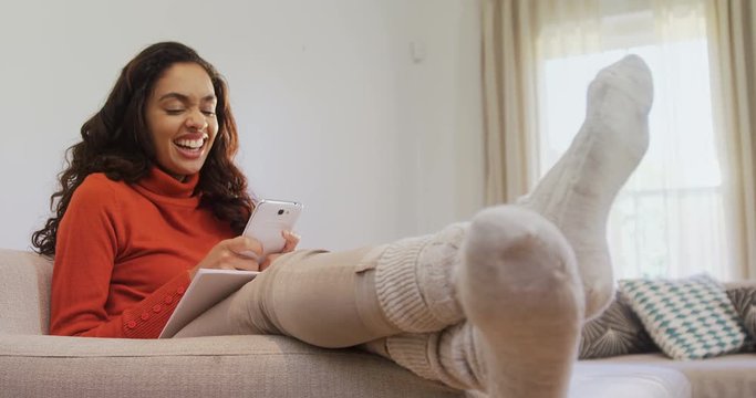 Woman sitting on sofa laughing while using her mobile phone  