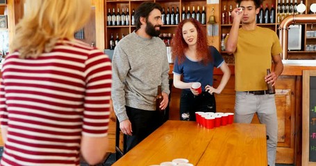 Friends playing beer pong on table in bar 