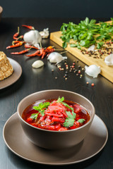 Red borscht soup with parsley in brown bowl top view, on black table.
