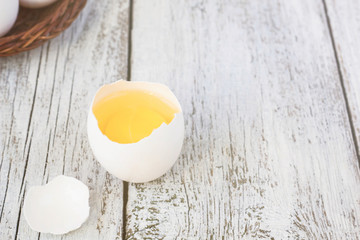 Broke One whole egg amongst white eggs in basket on a white wooden background