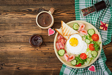 Breakfast on Valentine's Day - fried egg in the shape of a heart, toasts, sausage, bacon and fresh vegetables. English breakfast. Cup of coffee. Top view