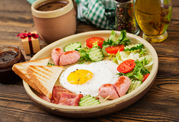 Breakfast on Valentine's Day - fried egg in the shape of a heart, toasts, sausage, bacon and fresh vegetables. English breakfast