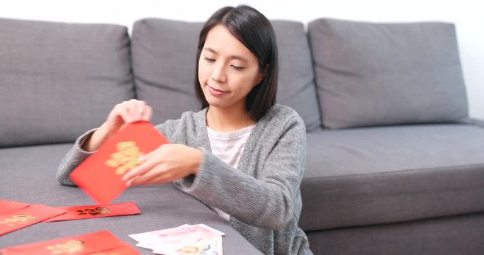 Woman putting money banknote into red packet at home