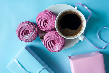 Pink marshmallows and a cup of coffee on a white saucer on a bright blue background. Gift boxes in pink and blue paper. Flat lay. Wedding table