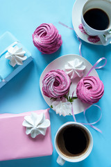 Pink marshmallows and  cups of coffee on a white saucer on a bright blue background. Gift boxes in pink and blue paper. Flat lay