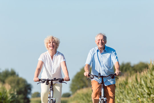 Full length of a senior active couple smiling and looking forward with confidence and serenity while riding bicycles in the countryside in summer