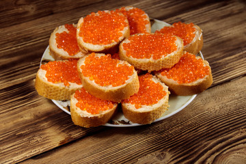 Sandwiches with butter and red caviar on wooden table