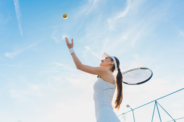 Woman playing tennis giving service throwing ball in the air