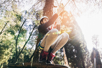 Happy school girl enjoying activity in a climbing adventure park on a sunny day