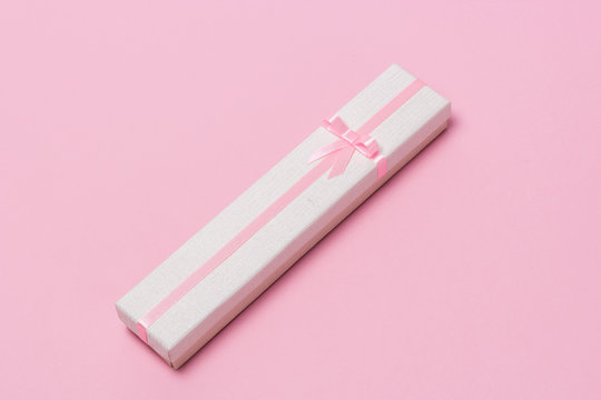 Long gift box with a pink ribbon and bow on a pink background