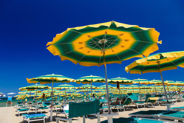 Colorful beach umbrella with sun beds on a sunny day. Rimini beach - Italy.