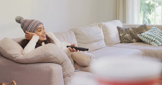 Happy woman in warm clothing lying on sofa watching television  