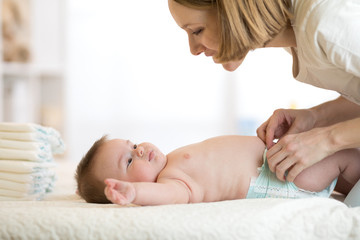 Obraz na płótnie Canvas Mother putting diaper on her happy baby