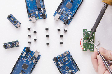 Six arduino  boards for robotics, 3D printing or developments and inventions. A man's hand with a soldering iron. You can see smoke from rosin. Learning boards in Fablab - Nano, Uno and Mega