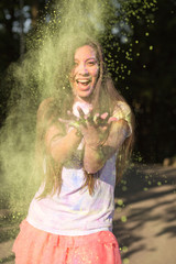 Expressive brunette woman wearing white shirt and pink skirt, tossing up dry Holi paint