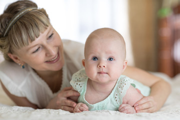 Mom and small daughter lying down on bed in nursery room. Mother embracing infant baby.