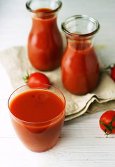 natural and healthy tomato juice in glass jars and a glass on a white wooden background. Top view