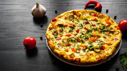 omelette with vegetables and olive in a plate on dark wooden background