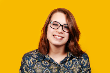 
Cheerful young woman in eyeglasses smiling at camera on orange background.