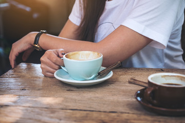 Closeup image of a woman holding latte coffee cup with Americano coffee cup on vintage wooden table in cafe